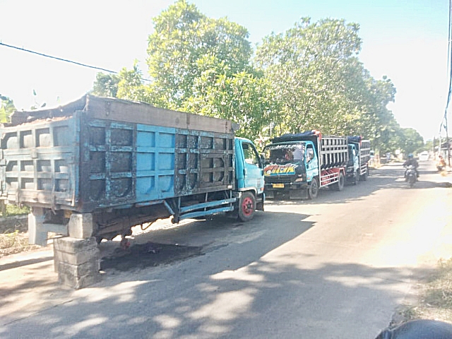 Truk muatan urukan yang mengalami patah as roda belakang akibat ban meletus.